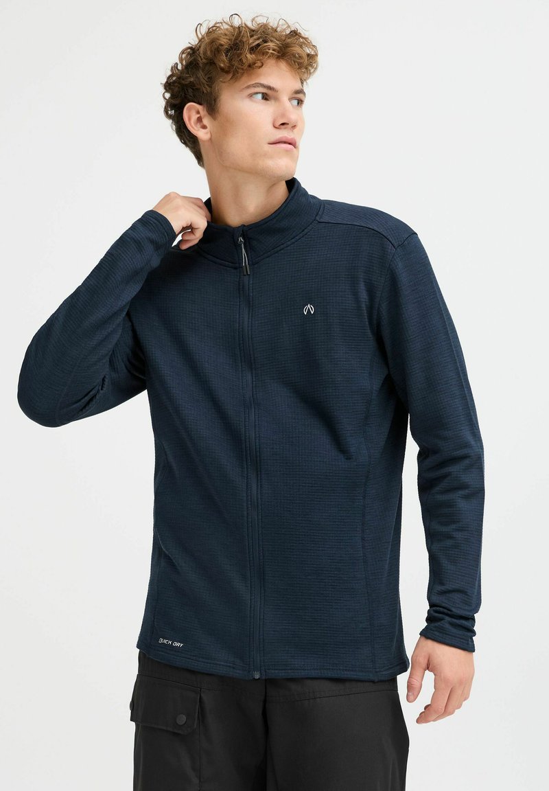 Marineblaues Zip-Jackett mit einem Gittermuster, Stehkragen und dezentem Logo. Eng anliegende Ärmel und ein gerader Saum runden das moderne Design ab.
