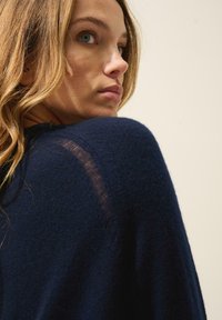 Pull en maille bleu marine avec une finition texturée, doté d'un col rond et d'un détail légèrement transparent sur l'épaule.