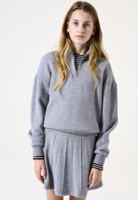 Grijze sweatshirt met hoge kraag en ritssluiting. Gecombineerd met een geplooide grijze rok. Gestreepte manchetten accentueren de mouwen. Zachte, gestructureerde stof.