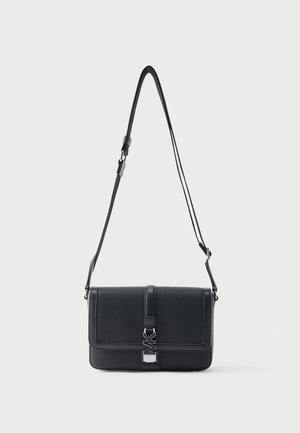 Czarna skórzana torba na ramię z regulowanym paskiem i srebrną klamrą z logo MK na przedniej klapie, na jasnym, jednolitym tle.