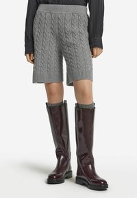 Graue, kabelgestrickte Shorts mit einem gerippten Bund, kombiniert mit knielangen burgunderfarbenen Stiefeln mit glänzender Oberfläche und flacher Sohle.