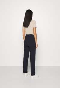 Marina högmidjade byxor med rak bendesign, mjukt tyg och elastisk midja, kombinerat med en ljusbeige åtsittande topp och vita sneakers.