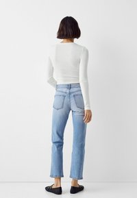 Vit långärmad topp, ljusblå högmidjade jeans med smal passform, något kortad längd och svarta platta skor.