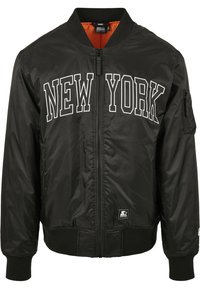 Chaqueta bomber negra con "NUEVA YORK" impresa en blanco en la parte delantera. Presenta un forro naranja y un cierre de cremallera al frente. Incluye puños y cintura acanalados.