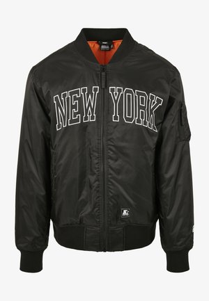 Giubbotto bomber nero con la scritta "NEW YORK" stampata in bianco sul davanti. Presenta una fodera arancione e una chiusura con zip. Include polsini e vita a coste.