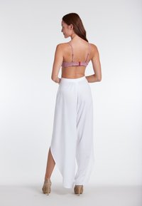 Roze gebloemde bralette met dunne bandjes, gecombineerd met hoge, vloeiende witte pantalons met zijknielen. Lichte tan hoge hakken.