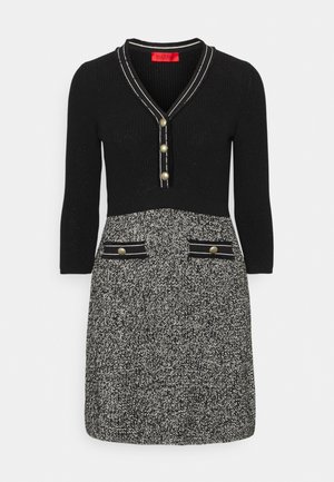 Zwart-witte gebreide jurk met driekwartmouwen, V-hals met knopen en twee voorkanten met knoopdetails.