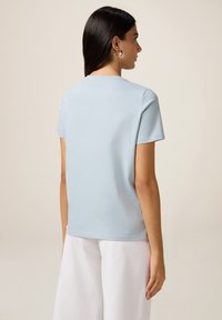 T-shirt en coton bleu clair avec un col rond, des manches courtes et une coupe décontractée. Texture lisse et design simple.