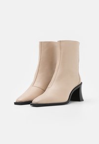 Stivaletti beige in pelle con punta appuntita e tacco scultoreo nero, caratterizzati da linee pulite e dettagli di cucitura minimali.