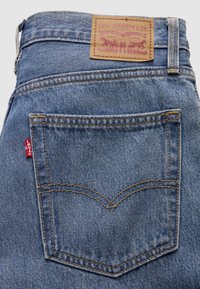 Bakficka på blå Levi's-jeans med karakteristisk bågformad söm, liten röd Levi's-tag och brunt lädermärke med Levi Strauss & Co.-märke ovanför midjebandet.