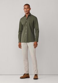 Olijfgroen overhemd met een button-down kraag, lange mouwen en witte knopen, gecombineerd met lichtbeige broek en bruine schoenen.
