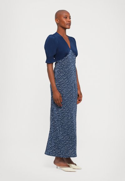 Navyblauwe jurk met korte pofmouwen, een aansluitende corsage en een lange rok, met een wit stippenpatroon door het geheel.