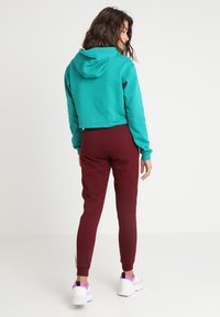 Tyrkis, avskåret hettegenser med hette, kombinert med mursteinsfargede joggebukser. Joggebuksene har ankelskjerf og er laget av mykt materiale. Hvite sneakers med rosa detaljer.