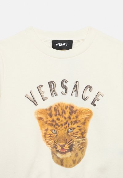 Maglietta bianca con stampa del volto di un cucciolo di leopardo e la parola Versace arcuata sopra l'animale nella zona del petto.