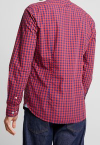 Camicia a maniche lunghe a quadratini rossi e blu, con colletto classico, polsini con bottone e orlo curvo, realizzata in cotone morbido.