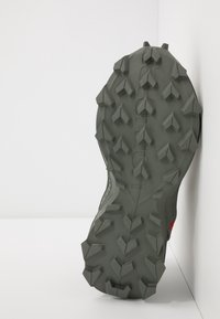 Šedá gumová podešev s agresivními, více směrovými hroty pro trakci. Obsahuje logo a hladký design okraje.