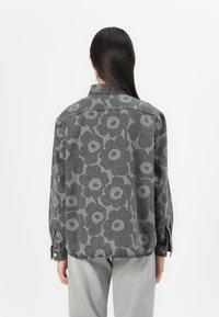Gray denim shirt with a large floral pattern in darker gray. Features a collar, button cuffs, and a slightly curved hem.