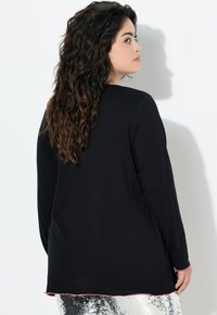 Czarna bluzka z długim rękawem i okrągłym dekoltem, z różowym szwem wzdłuż dołu, zestawiona z błyszczącymi srebrnymi spodniami. Materiał wydaje się być miękki.