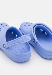 Jasnoniebieskie klapki Crocs z teksturowanej gumy, z tylnym paskiem, perforacjami dla wentylacji i podniesionym detalem logo.