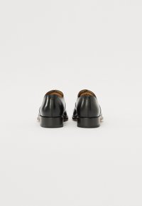 Zapatos de cuero negro con un acabado suave, tacón redondeado y un diseño minimalista. Presentan un forro interior en contraste de color marrón claro.
