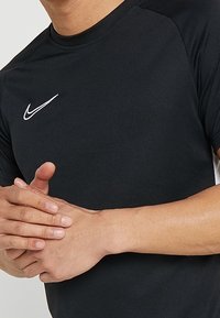 Camiseta deportiva negra de manga corta tipo raglán, con un logo blanco de Nike en el lado izquierdo del pecho y una textura de tela suave y transpirable.