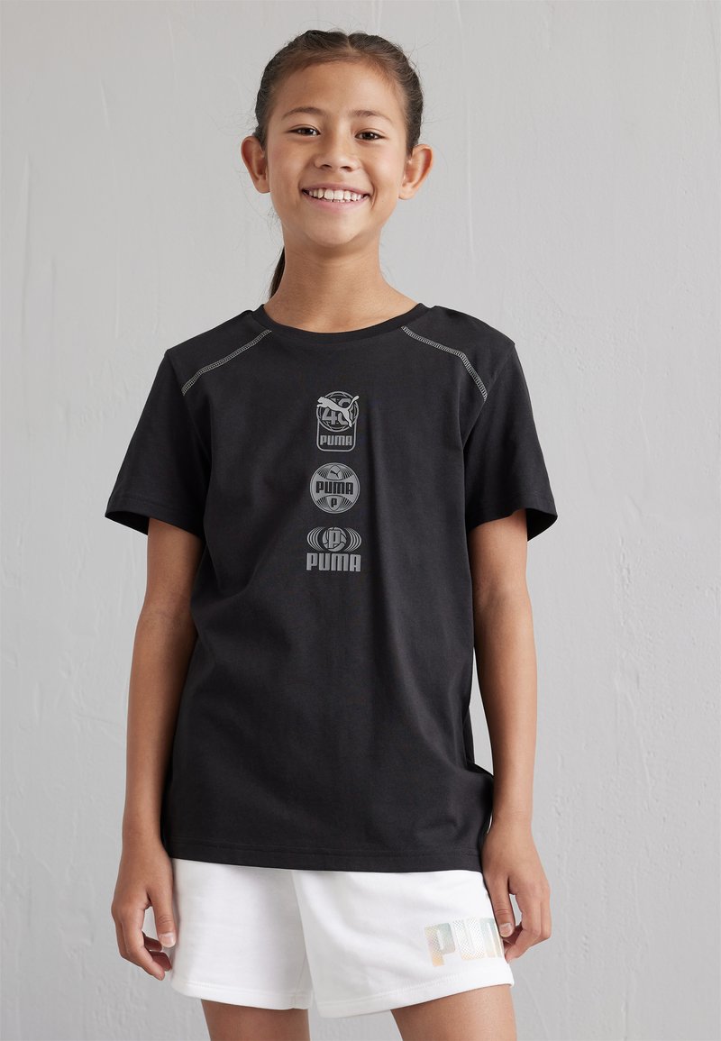 Camiseta negra de manga corta que presenta tres logotipos grises de Puma en el frente, con costuras reflectantes en los hombros. Combinada con pantalones cortos blancos.