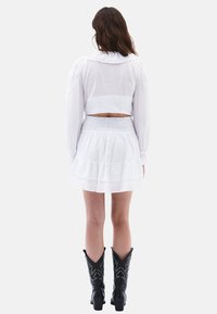 Blusa blanca corta con un gran cuello y mangas abullonadas, combinada con una mini falda blanca con volantes. Botas de vaquero negras con costuras decorativas.