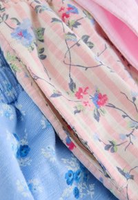 Tela suave con rayas rosas y blancas que presenta delicados patrones florales azules y rojos, superpuesta sobre tela azul claro con pequeñas flores azules.