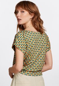 Värikäs lyhythihainen toppi, jossa on kukkakuosi oranssissa, keltaisessa ja vihreässä tummalla taustalla, valmistettu kevyestä kankaasta.