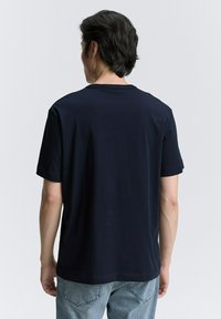 Tumši zila kokvilnas T-kreklu ar īsām piedurknēm, vienkāršs dizains, apaļa dekoltē un gluda tekstūra. Redzama izšūšana apakšmalā.