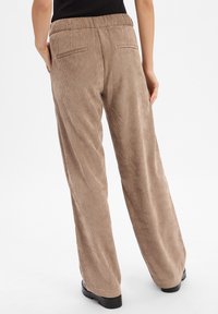Bruine corduroy broek met brede pijpen en een elastische tailleband, met twee achterzakken en een getextureerd ribbelpatroon.