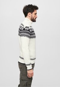 Pulover alb cu guler înalt, având un model geometric negru în partea superioară și accente negre la mansete și la tiv.