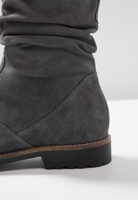 Šedá semišová kotníková bota s volným designem, zakulacenou špičkou, texturovaným povrchem a nízkým masivním černým gumovým podpatkem.