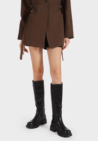 Stivali neri in pelle al ginocchio con finitura liscia, punta rotonda, suola spessa e cerniere laterali per una facile calzata.