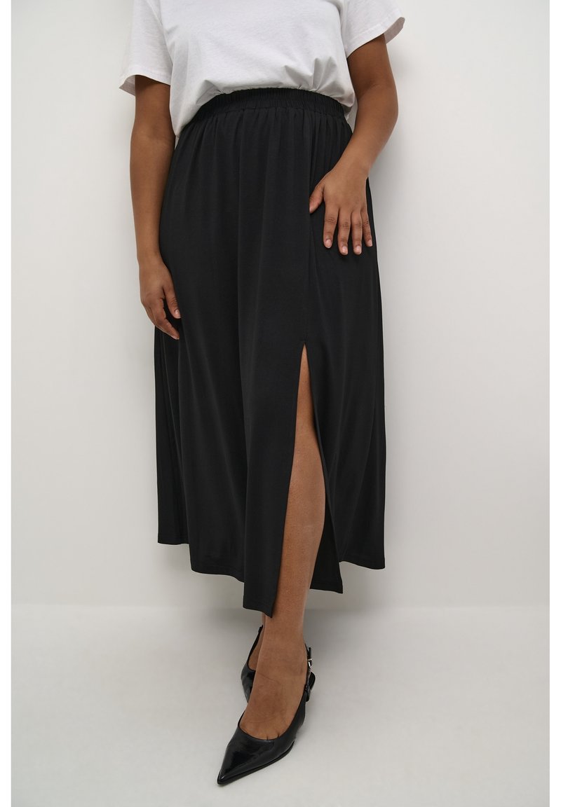 Zwarte midi-rok met een zijspleet, gemaakt van lichtgewicht stof. Elastische tailleband en een gladde textuur. Gecombineerd met puntige zwarte hakken.