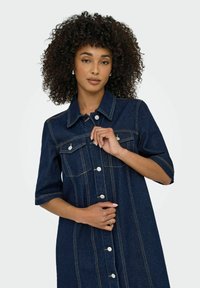 Denimklänning med korta ärmar, mörkblå f�ärg, silverfärgade knapppryttare och ljusa sömmar. Har två bröstfickor och en krage.