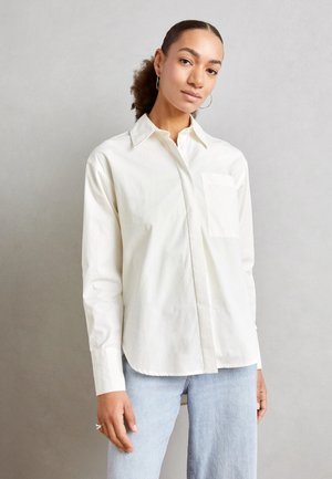 Witte, langärmelige shirt van lichtgewicht katoen, met een klassieke kraag, één borstzak en een gebogen zoom. Gekleed met lichte jeans.