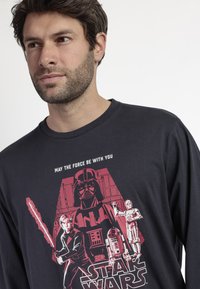 Camiseta negra de manga larga con un estampado gráfico de personajes de Star Wars, letras rojas y un cuello redondo.