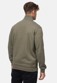 Olivengrøn fleece-pullover med høj krave, ribbede manchetter og kant. Subtil vandret struktur, afslappet pasform og ingen synlig branding.