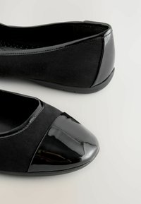 Zwarte balletschoenen met een matte suede bovenkant en een glanzende lakneus, met een laag profiel en een flexibele rubberen zool.