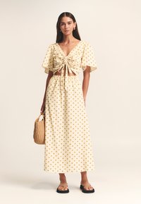 Dvodelna obleka: kratka majica in maksi krilo v svetlo rumeni barvi z zlatimi pikami, zavezana spredaj, kratkimi rokavi in elastičnim pasom. Tkan torbica.