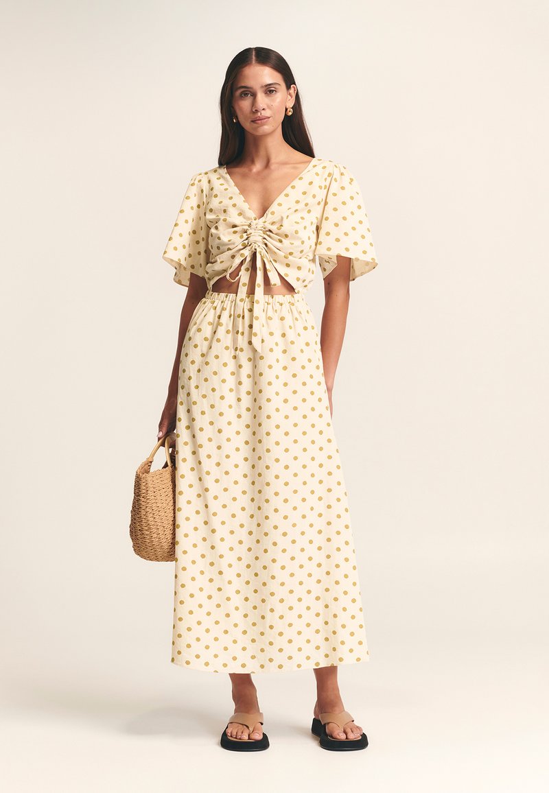 Dvodelna obleka: kratka majica in maksi krilo v svetlo rumeni barvi z zlatimi pikami, zavezana spredaj, kratkimi rokavi in elastičnim pasom. Tkan torbica.