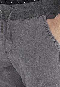 Pantalones de chándal grises con una cinturilla acanalada, cierre con cordón, bolsillos laterales y una textura suave. Costuras resistentes a lo largo de las costuras.