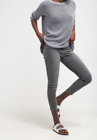 Harmaa neulepaita, kapeat harmaat farkut ja hopeanväriset sandaalit, joissa on kaksi hihnaa. Neule on väljä ja farkut ovat nilkkapituiset ja istuvat.