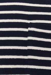 Merino neulekangas tummansinisellä pohjalla, jossa on vaakasuoria valkoisia raitoja. Sisältää pienen taskuyksityiskohdan. Tekstuuri näyttää pehmeältä ja hieman joustavalta.