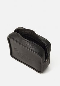 Bolso de piel negra con superficie texturizada, forma rectangular, cierre de cremallera y logotipo grabado en la parte frontal. El interior está forrado con tela.