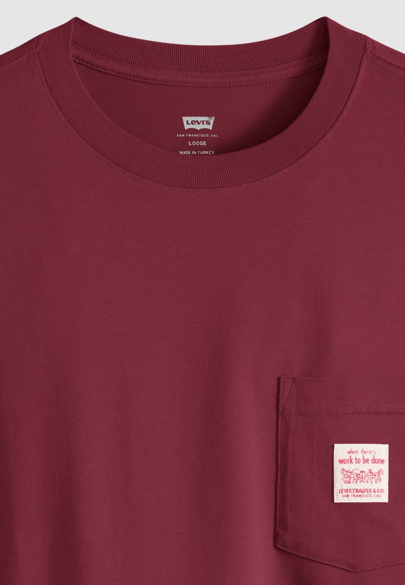 T-shirt ampio color marrone scuro di Levi's con scollo rotondo e tasca frontale con etichetta bianca con testo e grafica rossa.