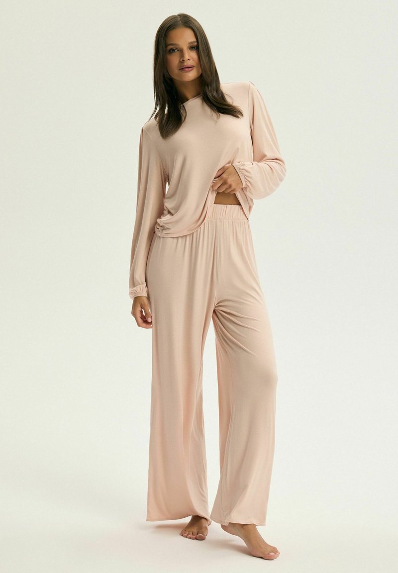 Jasnoróżowy zestaw odzieży domowej z luźną bluzą na długim rękawie z dekoltem w serek oraz spodniami o szerokich nogawkach z miękkiego materiału. Prosty design.