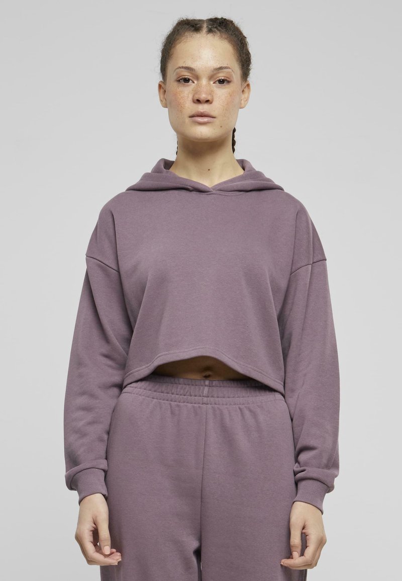 Felpa viola a maniche lunghe e con cappuccio, realizzata in materiale morbido. Abbinata a pantaloni della tuta con cintura elastica coordinati.