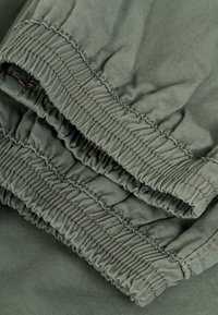 Primer plano de tela verde oliva con bordes elásticos fruncidos y costuras detalladas en la manga o puño de una prenda.